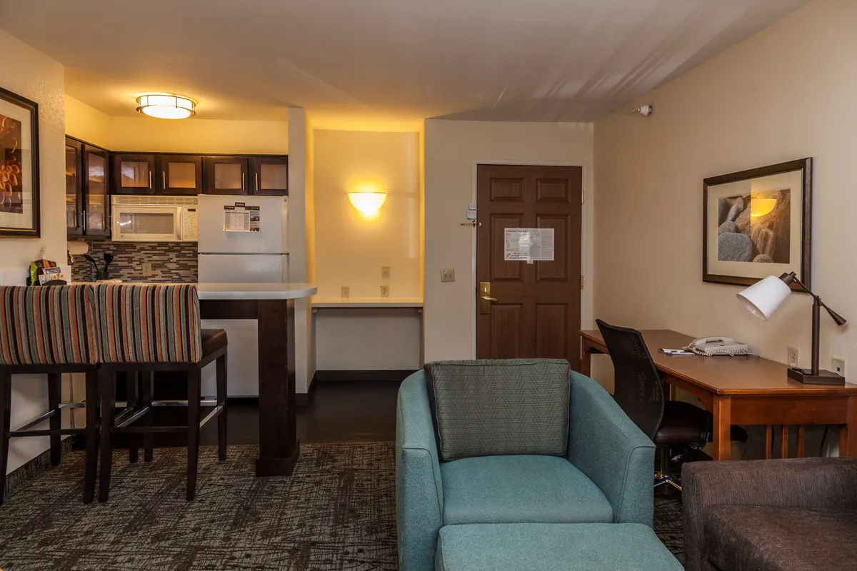 The image showcases a warm and inviting open-plan living space with a modern kitchenette, a comfortable seating area perfect for relaxing, a desk ideal for remote work or planning adventures, and the welcoming entrance. The space is well-lit and thoughtfully arranged, offering both comfort and functionality for guests.