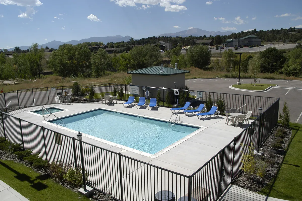A lively heated outdoor swimming pool is surrounded by lush greenery, lounge chairs, and a pool house, creating a vibrant setting for family fun and relaxation. The image evokes scenes of swimming, sunbathing, and gathering with loved ones after a day of exploring local attractions.