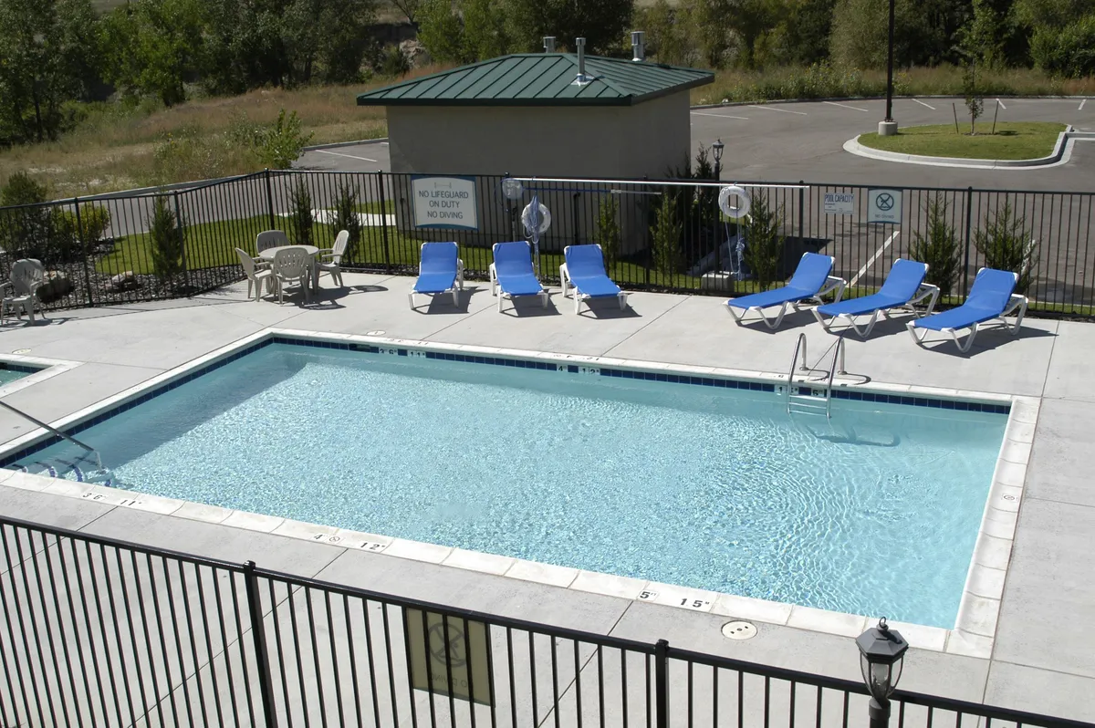The image features an inviting swimming pool ringed by lounge chairs and greenery, with a modern pool house in view. Groups and families are shown swimming, sunbathing, and mingling poolside, creating an atmosphere of fun and community perfect for social activities or post-adventure relaxation.